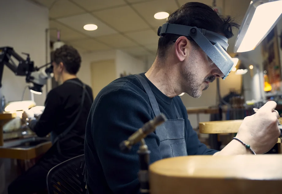 Orfebre trabajando una joya con herramientas de precisión en el taller